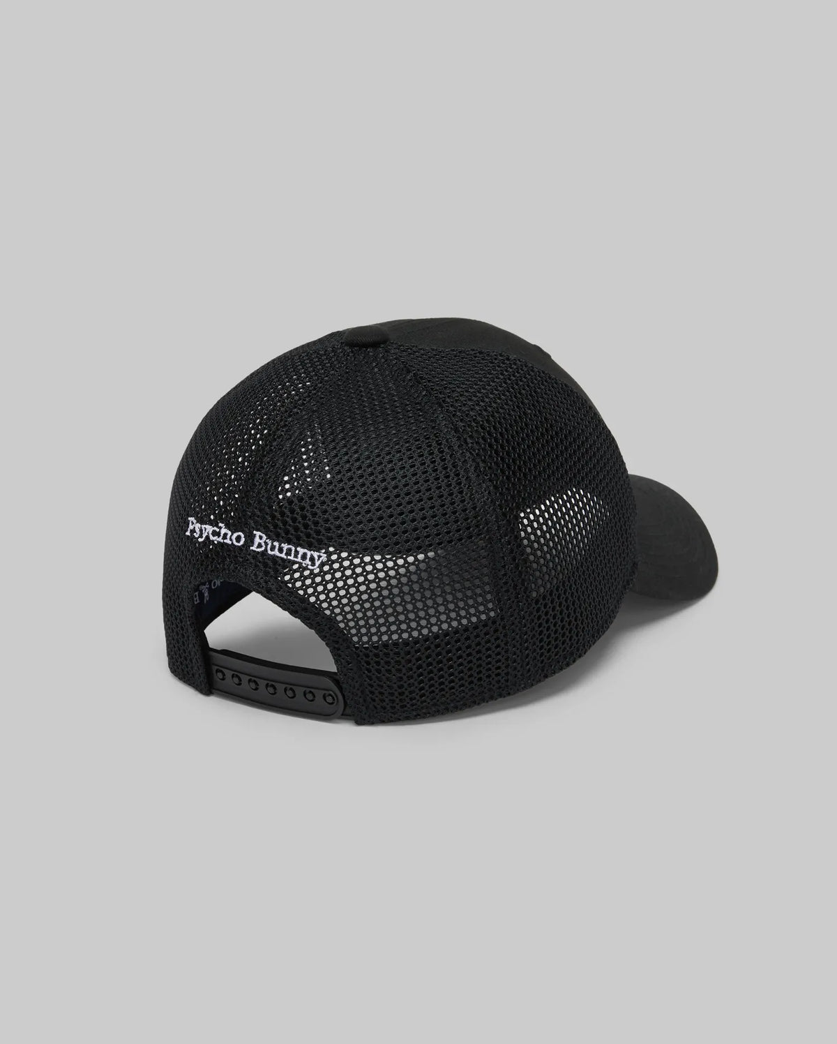 The KIDS DARIO TRUCKER CAP (KO1500009) by Psycho Bunny is shown from the back, featuring black mesh, an adjustable snap-back closure, and "Psycho Bunny" embroidered in white above the opening, set against a plain gray background.