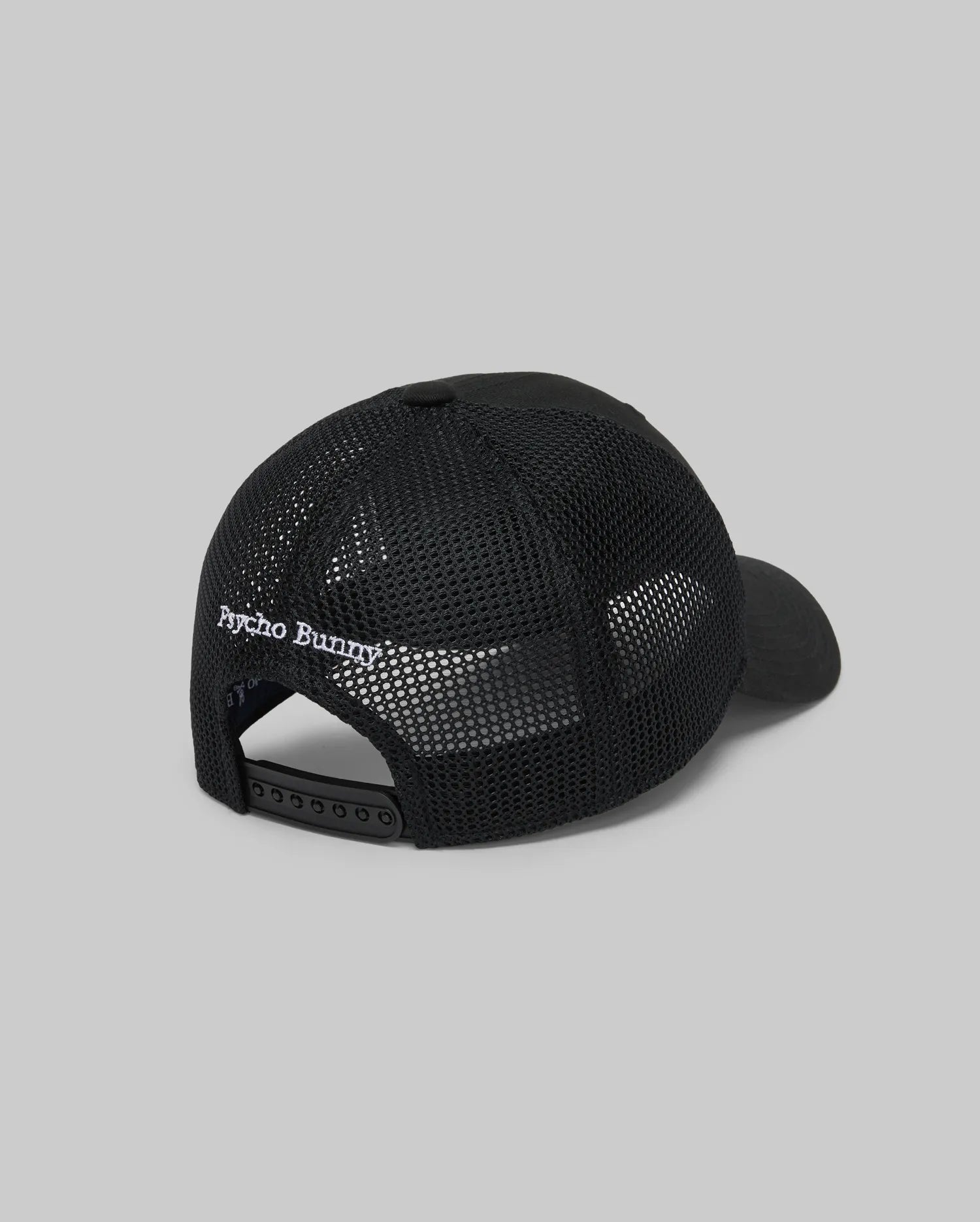 The KIDS DARIO TRUCKER CAP (KO1500009) by Psycho Bunny is shown from the back, featuring black mesh, an adjustable snap-back closure, and "Psycho Bunny" embroidered in white above the opening, set against a plain gray background.