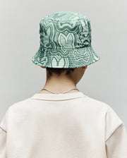 A person is seen from behind in a light beige sweatshirt and the Psycho Bunny KIDS CHUCK REVERSIBLE BUCKET HAT (KO1500015), which features a green pattern and SPF protection, against a plain gray background.