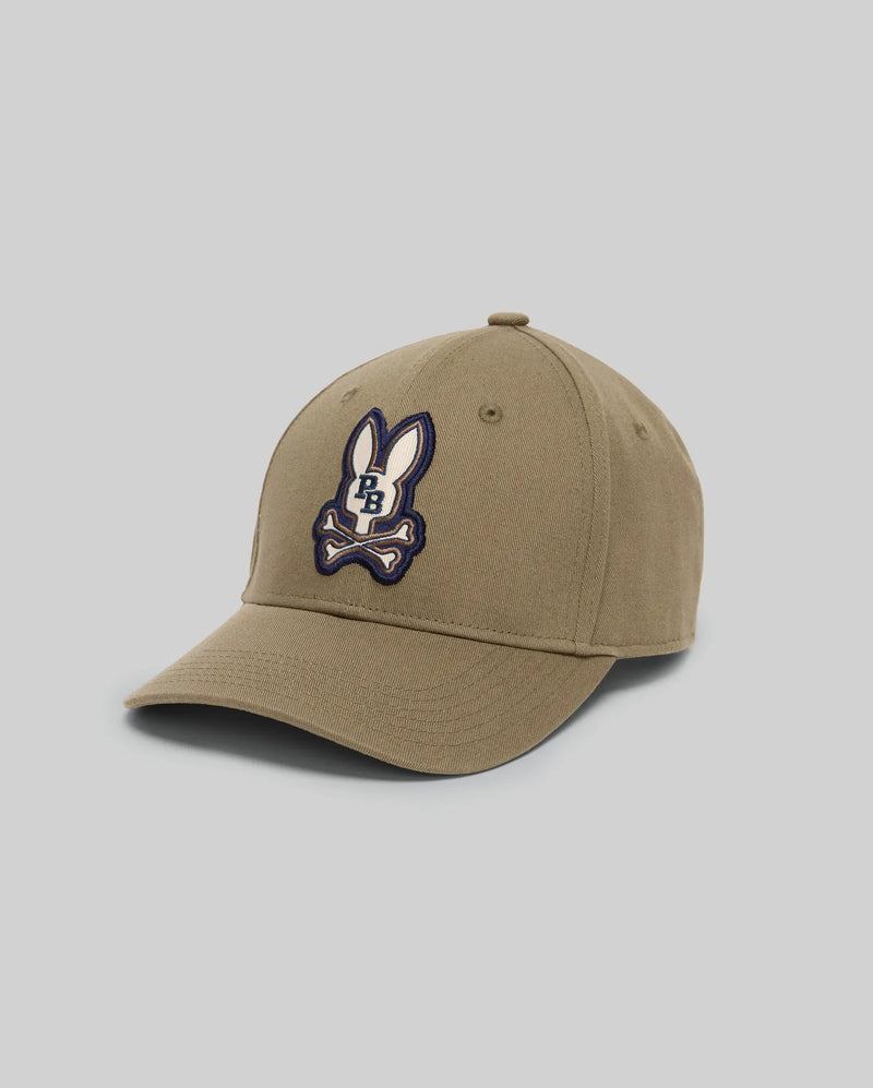 The KIDS WADE BASEBALL CAP - KO1500016 by Psycho Bunny is a khaki cotton twill cap with an embroidered Bunny logo above crossed bones on the front panel, shown against a plain light grey background.