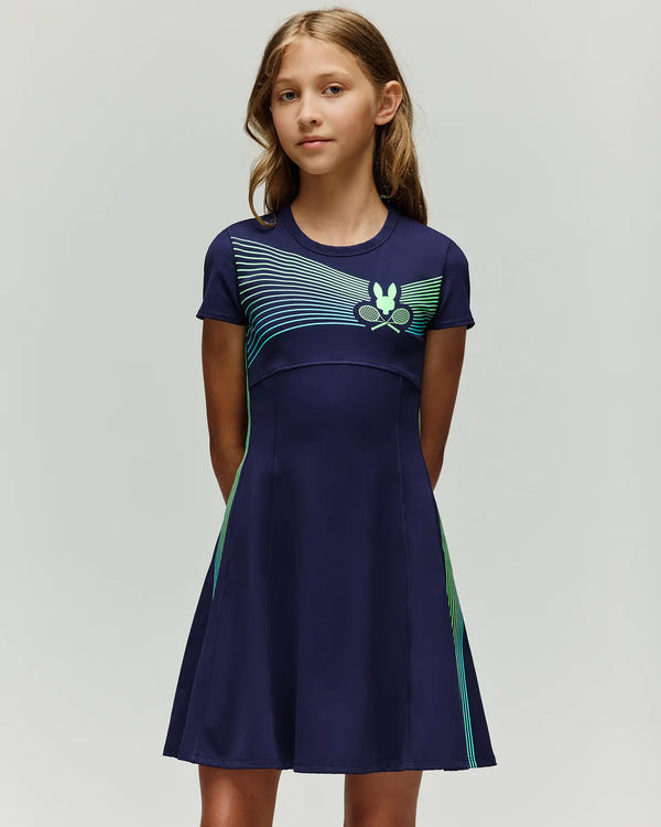 A young girl with long light brown hair stands facing forward, hands behind her back, wearing the Psycho Bunny RETAIL BALL CREW GIRLS DRESS (EN) - KO2000005: a navy short-sleeve dress with light blue and green diagonal stripes and a butterfly logo.