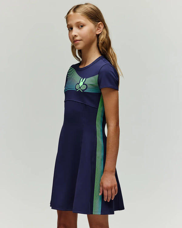 A young girl with long, light brown hair wears the Psycho Bunny RETAIL BALL CREW GIRLS DRESS (EN) - KO2000005, a navy blue short-sleeve dress featuring green and blue stripe accents and a chest graphic, standing against a plain light background.