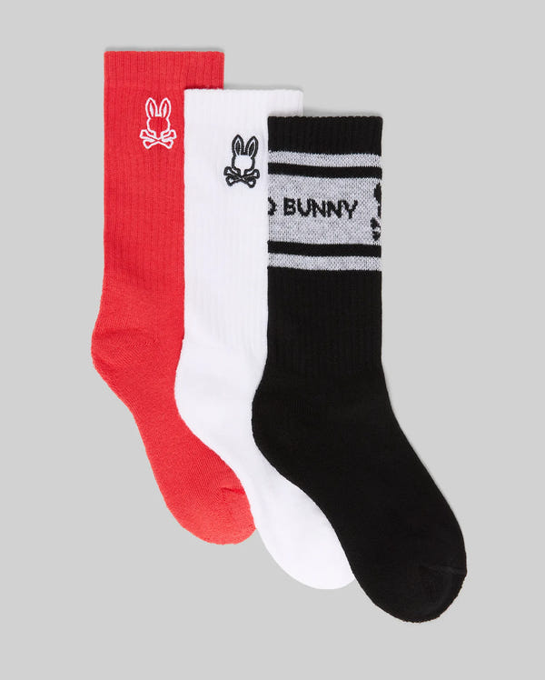 The Psycho Bunny KIDS 3 PACK SPORT SOCK (KO2200001) includes red, white, and black crew socks in soft Pima cotton with spandex. Each pair has a bunny logo; the black pair features white stripes and "BUNNY" text. Light gray background.