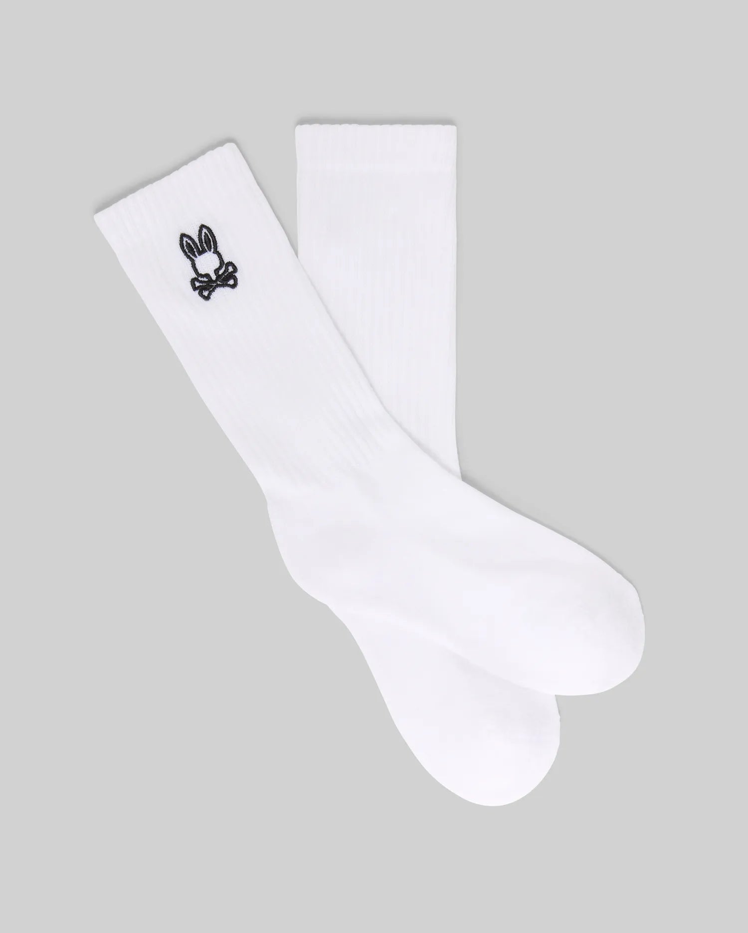 The Psycho Bunny KIDS 3 PACK SPORT SOCK (KO2200001) includes white crew socks made with soft Pima cotton and spandex, each featuring a small black bunny skull and crossbones logo near the top. Displayed on a gray background.