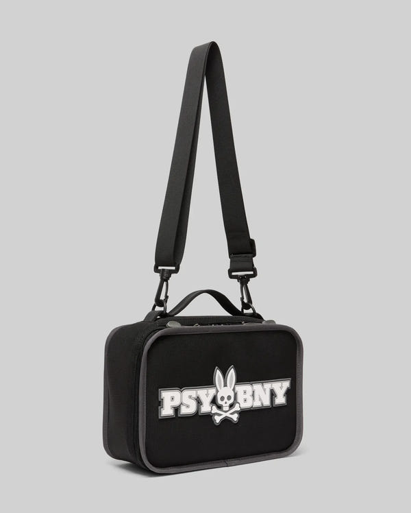The PSYCHO BUNNY LUNCH BOX - KO2400002 by Psycho Bunny is a black rectangular bag with a handle and adjustable shoulder strap, featuring a white "PSYBNY" logo and a silicone Bunny skull and crossbones on the front. Background: light gray.