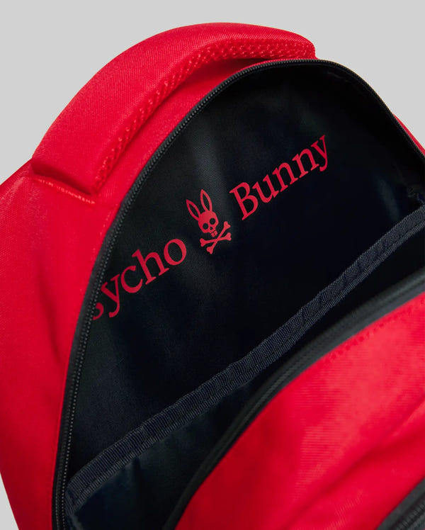 A close-up of an open KIDS PSYCHO BUNNY BACKPACK - KO2400004 by Psycho Bunny shows a black interior featuring pink "Psycho Bunny" text and the signature bunny skull-and-crossbones logo printed inside.