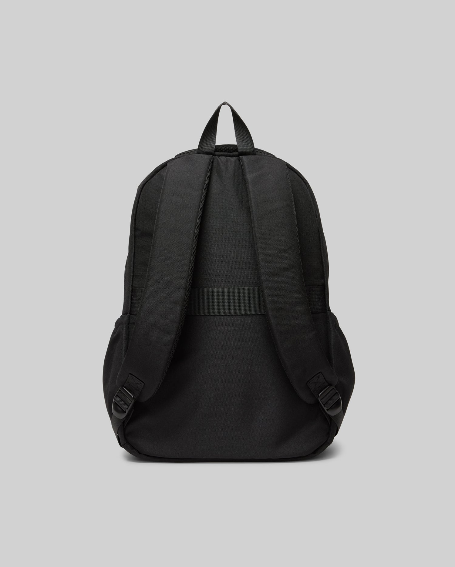 The Psycho Bunny KIDS PSYCHO BUNNY BACKPACK (KO2400004) is shown from the back, highlighting its padded adjustable shoulder straps, top handle, and plain durable canvas design against a light gray background.