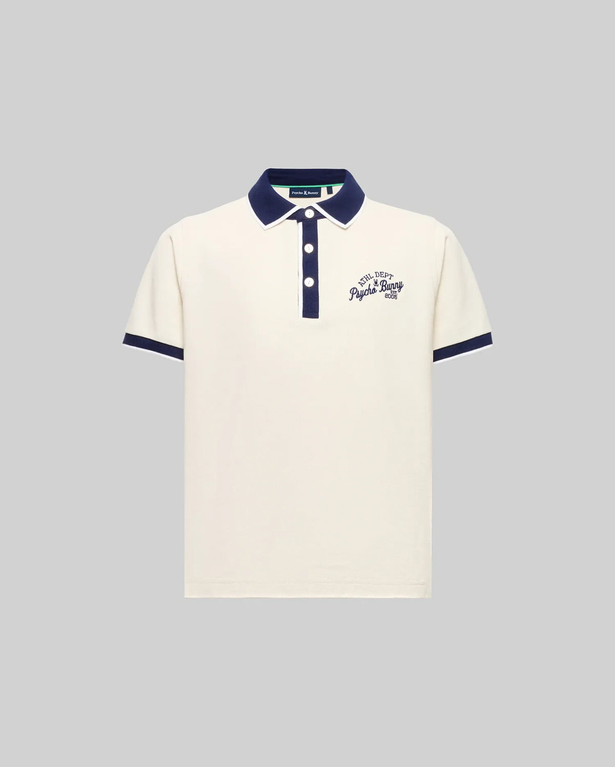 The KIDS MATTEO PIQUE POLO (KT0100021) by Psycho Bunny is an off-white, short-sleeved Pima cotton polo with navy collar and cuffs, mother-of-pearl buttons, and embroidered chest text. Displayed on a plain grey background.