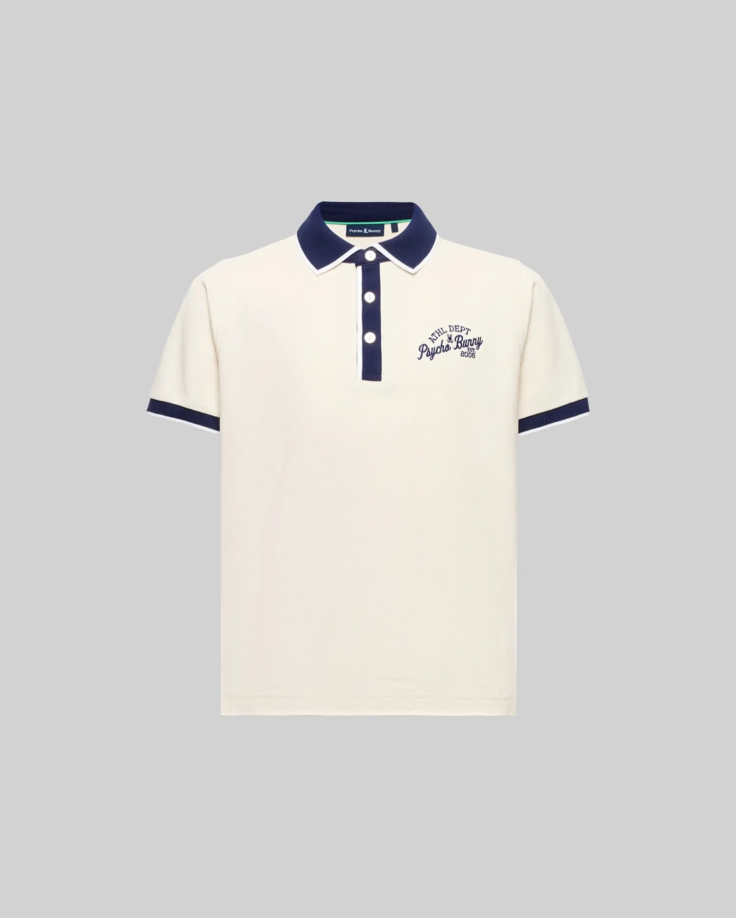 The KIDS MATTEO PIQUE POLO (KT0100021) by Psycho Bunny is an off-white, short-sleeved Pima cotton polo with navy collar and cuffs, mother-of-pearl buttons, and embroidered chest text. Displayed on a plain grey background.