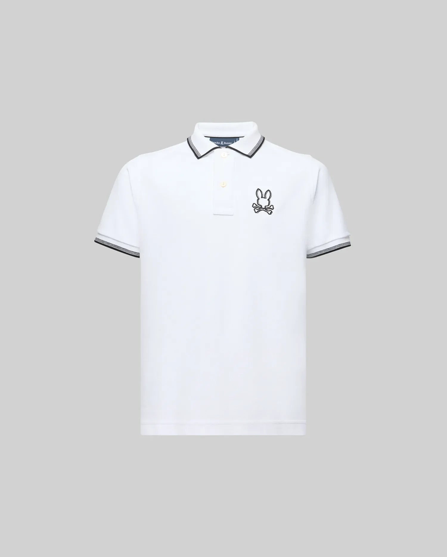 The Psycho Bunny KIDS JUDE PIQUE POLO (KT0100027) is a white Pima cotton short-sleeve polo with black trim on the collar and sleeve cuffs and an embroidered bunny logo on the left chest, shown against a plain gray background.