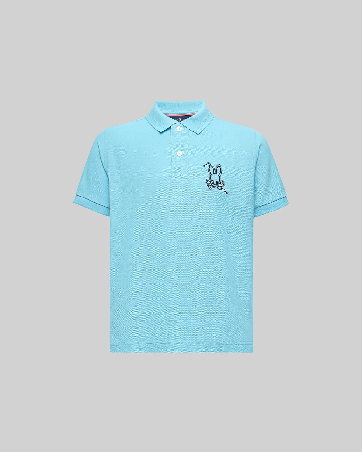 The KIDS CYRUS PIQUE POLO (KT0100031) by Psycho Bunny is a light blue short-sleeve Pima cotton polo with a two-button placket and an embroidered cartoon bunny on a skateboard, shown on a plain gray background.