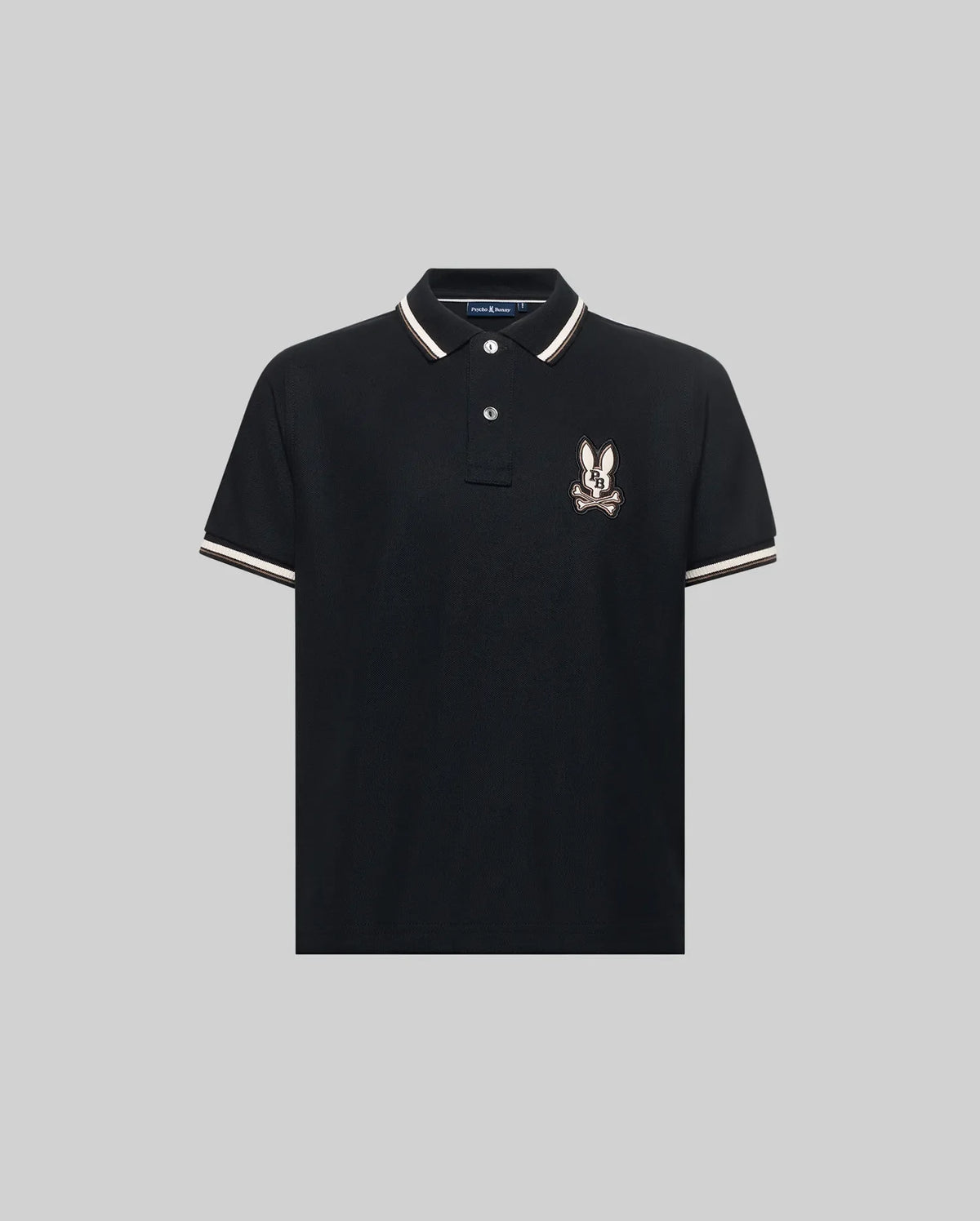 The Psycho Bunny KIDS WADE PIQUE POLO (KT0100032) is a black Pima cotton polo with colorblock tipping on the collar and sleeves, plus an embroidered cartoon rabbit logo on the left chest, shown on a light gray background.