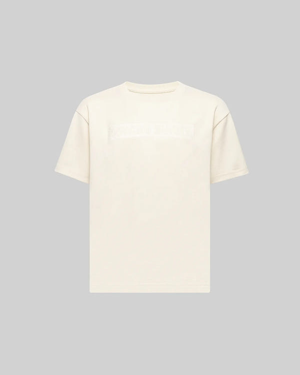 The KIDS ZAYN OVERSIZED GRAPHIC TEE (KT0200001) by Psycho Bunny is a relaxed-fit, off-white, short-sleeve 100% cotton tee featuring a subtle chest patch with indistinct text, shown on a light grey background.