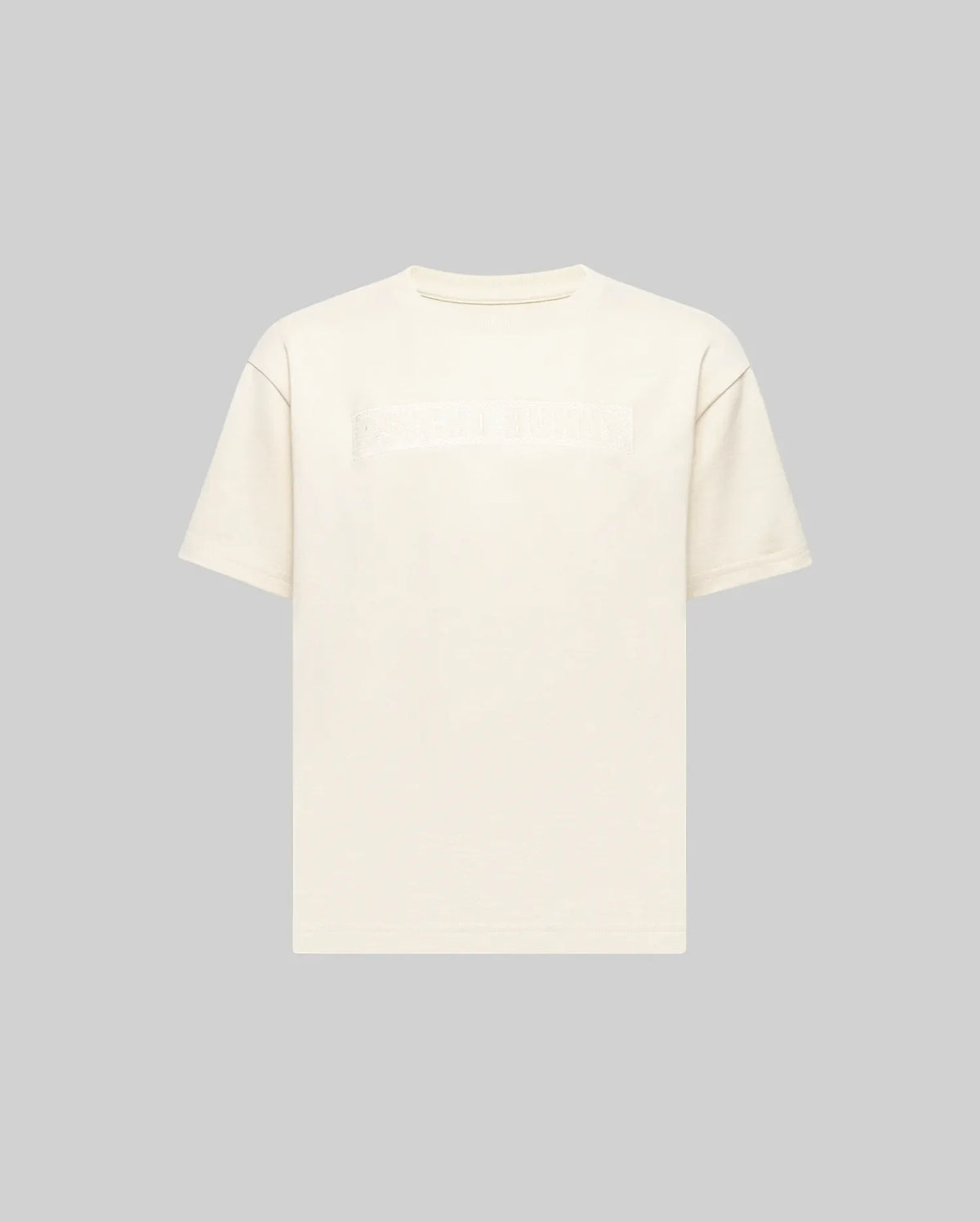 The KIDS ZAYN OVERSIZED GRAPHIC TEE (KT0200001) by Psycho Bunny is a relaxed-fit, off-white, short-sleeve 100% cotton tee featuring a subtle chest patch with indistinct text, shown on a light grey background.