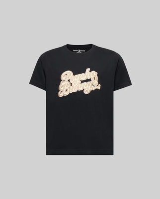 The KIDS ELIAS GRAPHIC TEE (KT0200013) by Psycho Bunny is a black Pima cotton t-shirt featuring "Psycho Bunny" in bold beige script across the chest, adding a retro touch on a plain gray background.