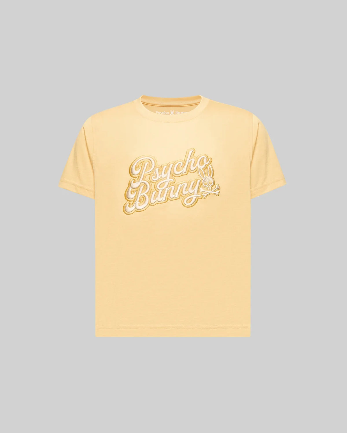 The KIDS ELIAS GRAPHIC TEE (KT0200013) by Psycho Bunny is a light yellow, retro-style short-sleeve Pima cotton t-shirt featuring "Psycho Bunny" in large white script and a bunny with a carrot, shown on a plain gray background.
