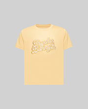 The KIDS ELIAS GRAPHIC TEE (KT0200013) by Psycho Bunny is a light yellow, retro-style short-sleeve Pima cotton t-shirt featuring "Psycho Bunny" in large white script and a bunny with a carrot, shown on a plain gray background.