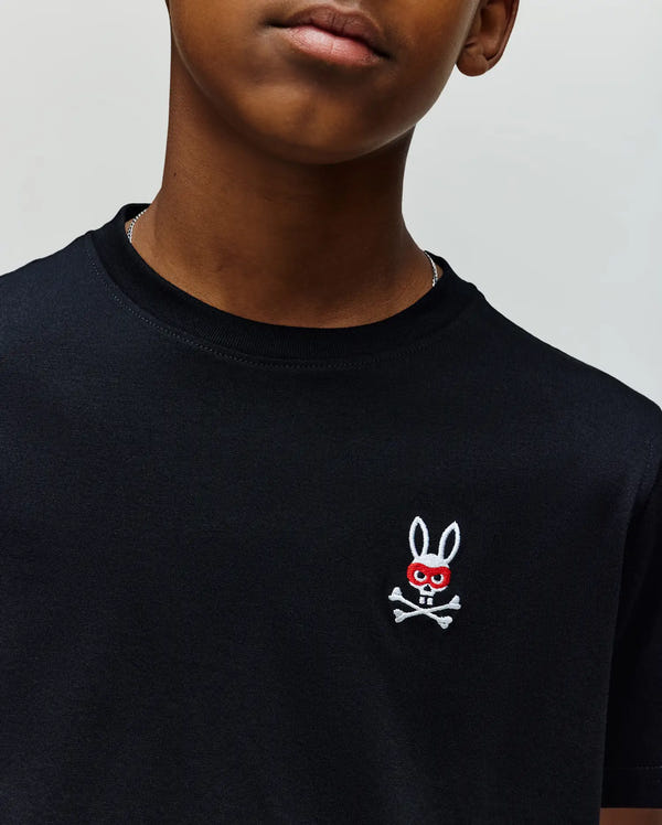 A child wears the Psycho Bunny KIDS MISCHIEF BUNNY TEE (KT0200023), a black Pima cotton shirt with a red skull and bunny ears logo on the chest. Photo is cropped to show only the lower face and upper torso.