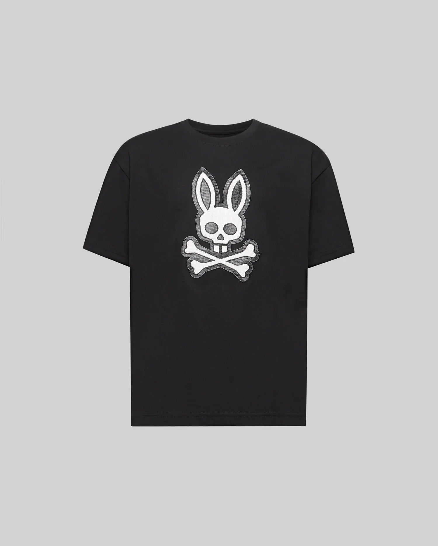 The Psycho Bunny KIDS RYDER OVERSIZED FIT TEE (KT0200056) is a black premium tee crafted from soft Pima cotton, featuring a white embroidered Bunny skull with bunny ears above crossed bones against a gray background.