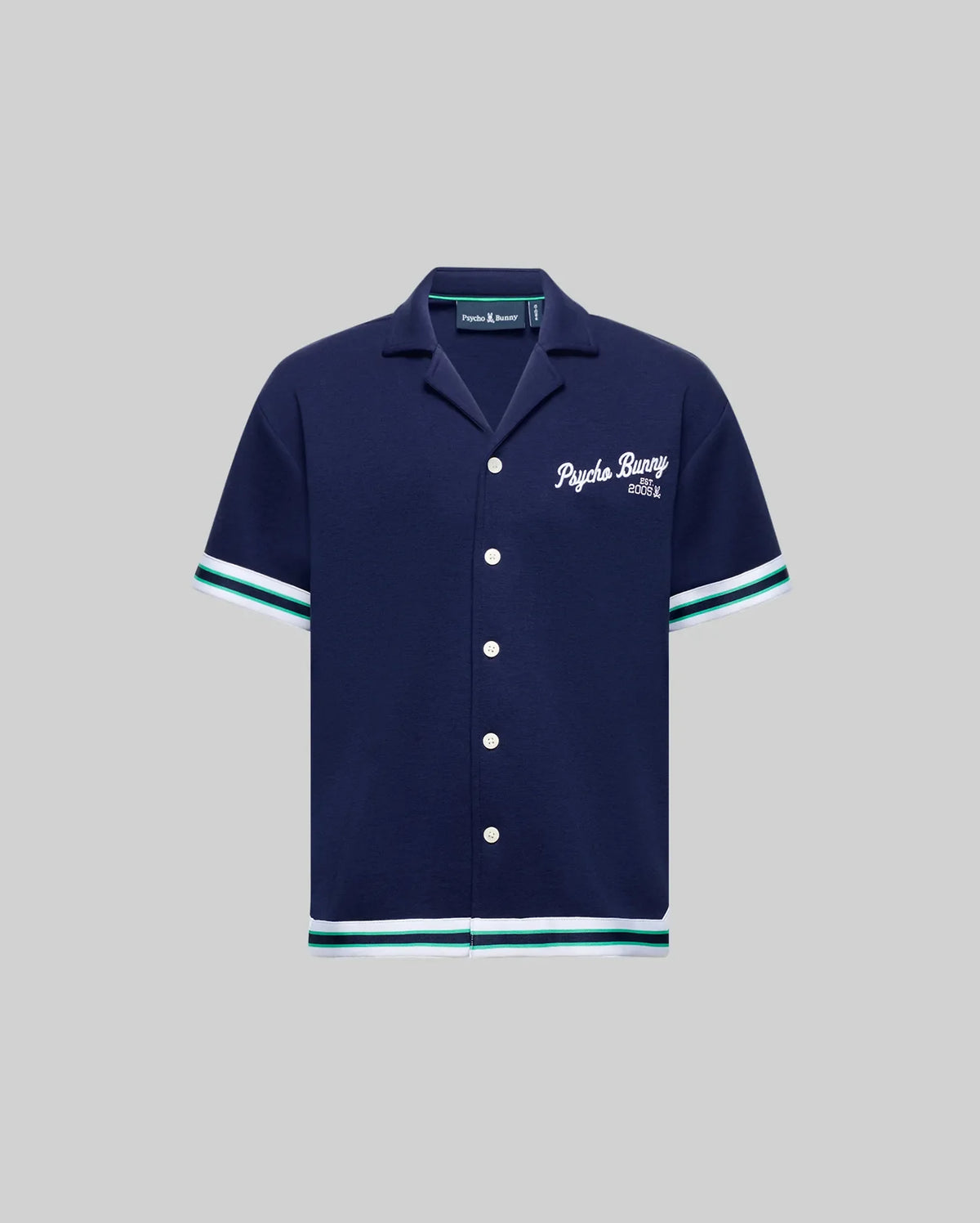 The Psycho Bunny KIDS BASIL TAPED CAMP COLLAR SHIRT (KT0500007) is a navy cotton-modal blend with white buttons, white and teal sleeve/hem trim, and "Psycho Bunny Est. 2005" embroidered in white on the left chest. Shown on gray background.