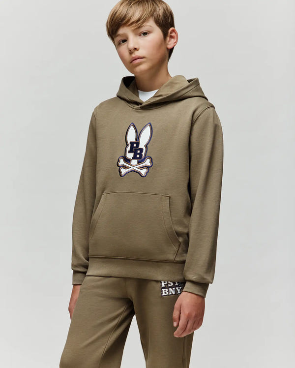 A boy wears the Psycho Bunny KIDS WADE CORD PATCH HOODIE - KT0500031 and matching pants, both in olive green with a bunny and crossbones logo on the hoodie and "PS BNY" lettering on the pants, standing against a plain light background.
