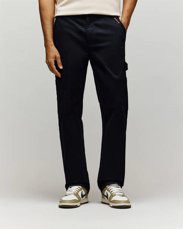 A person wearing Psycho Bunny MENS RUSSELL CARPENTER PANT - MB0600005 in a regular fit, paired with a light shirt and white sneakers with green accents, stands against a plain light background. Only the lower half is visible.