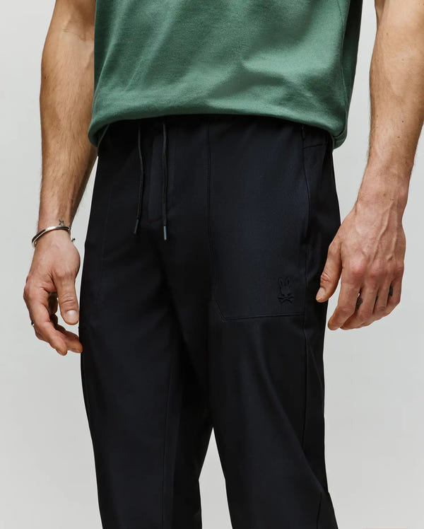 A person wears Psycho Bunny’s MENS BEN TECH JOGGER PULL ON (MB0600013) in black polyester spandex with a small embroidered bunny logo on the left pocket, standing with arms relaxed by their sides.