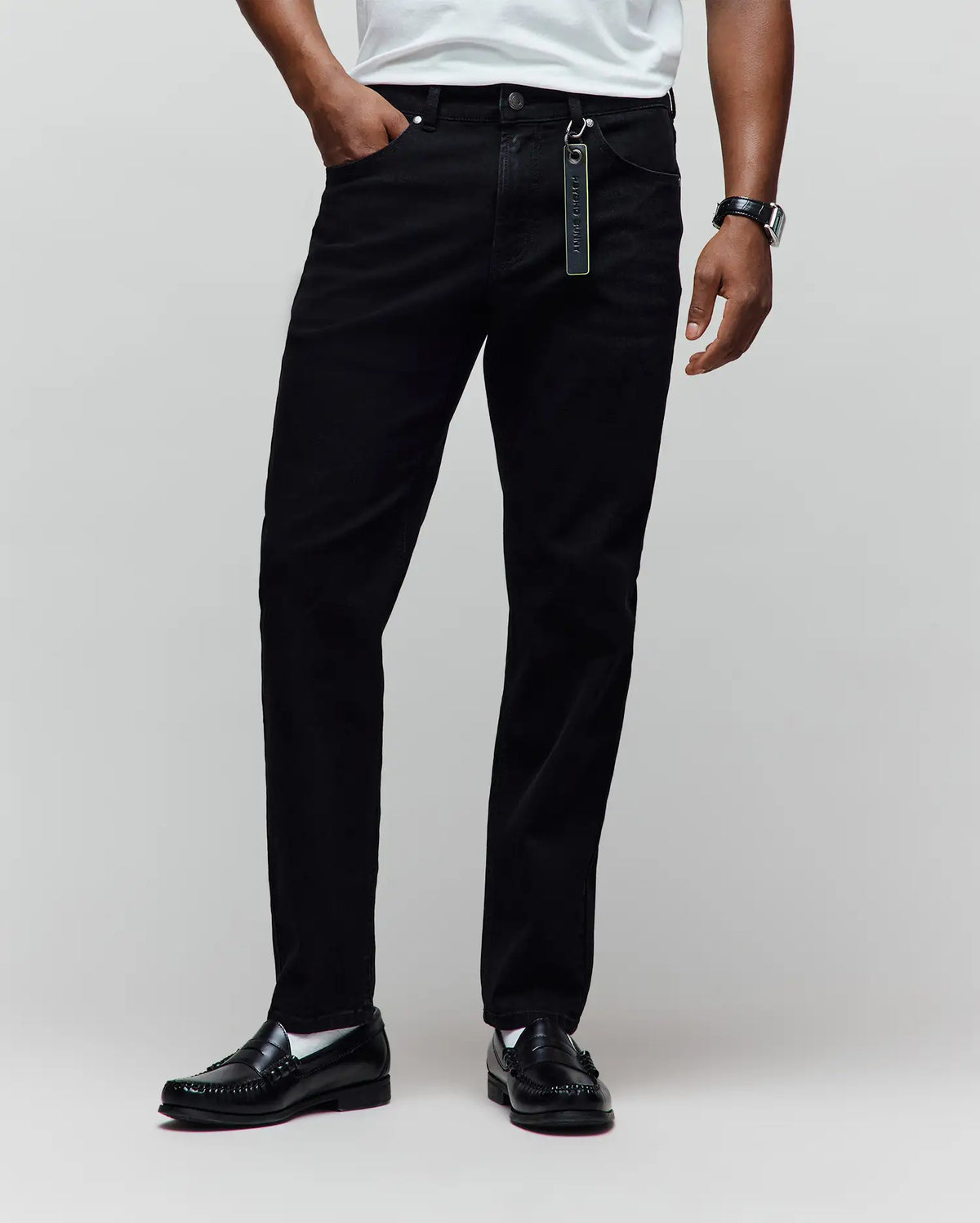 Black Mens Emerson Denim Pant, classic fit, with a visible denim texture and a vibrant green Psycho Bunny keychain attached to the front belt loop.