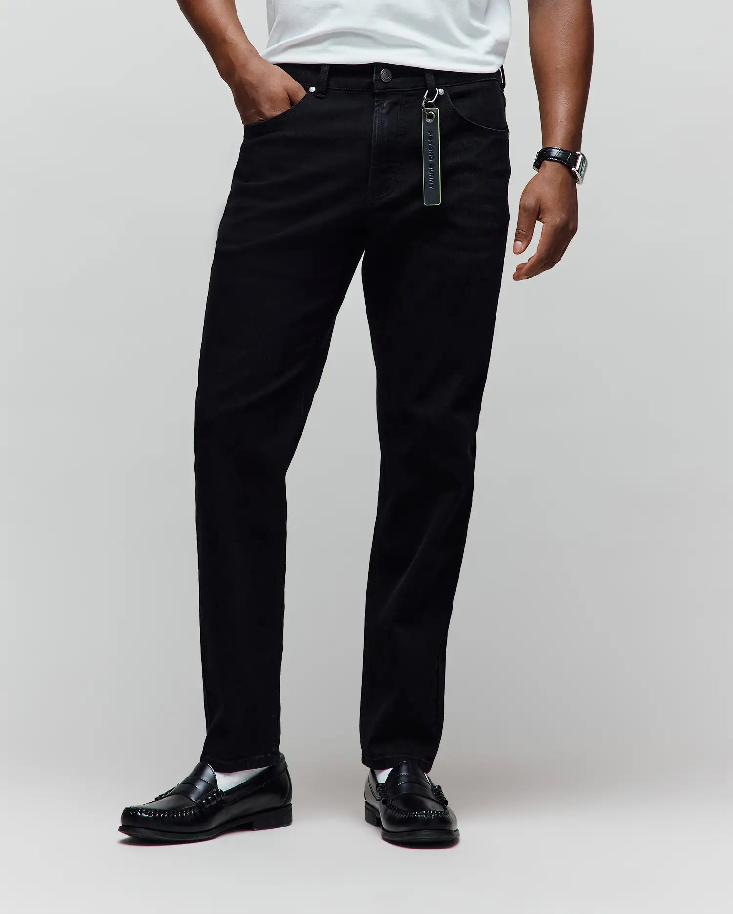 Black Mens Emerson Denim Pant, classic fit, with a visible denim texture and a vibrant green Psycho Bunny keychain attached to the front belt loop.