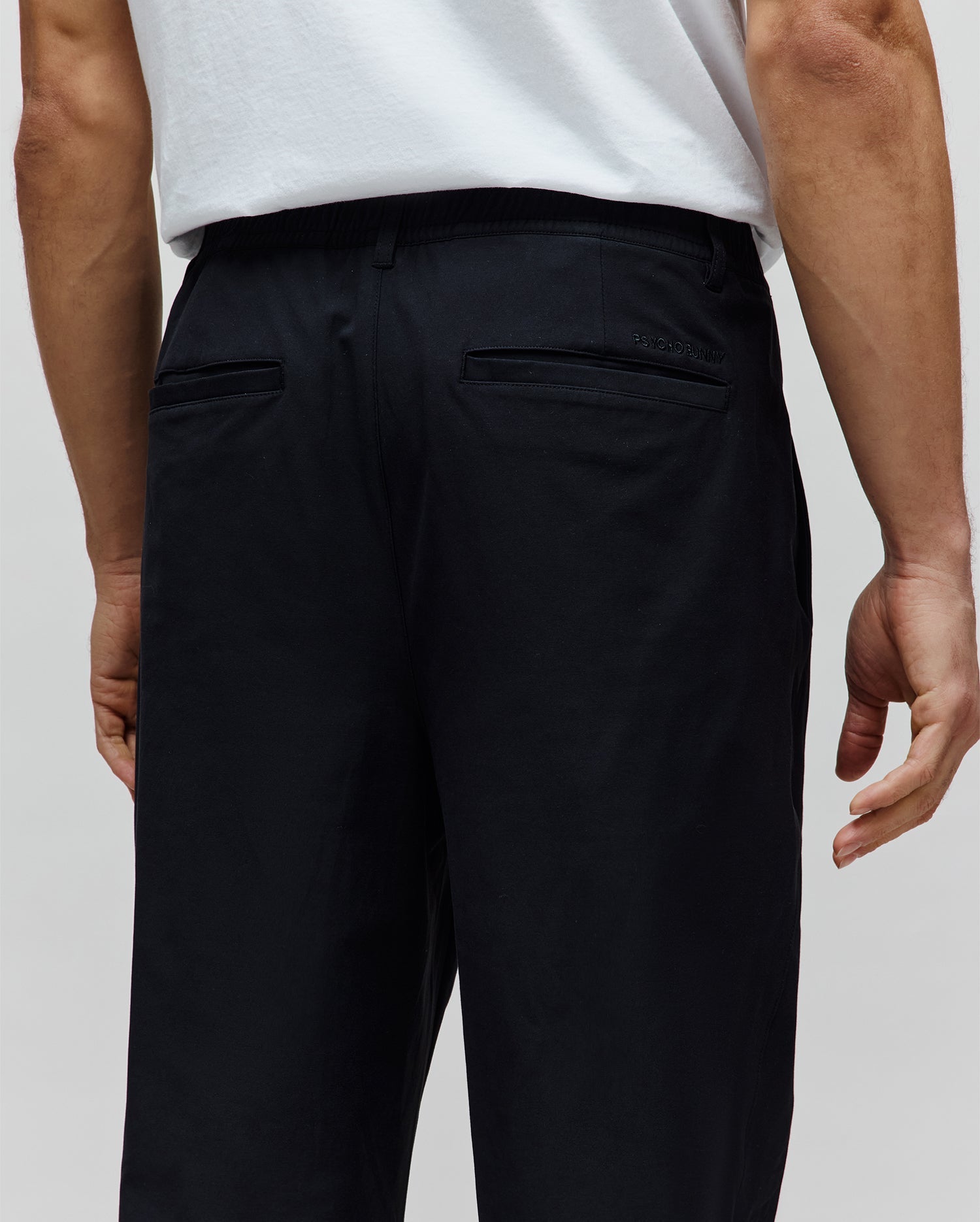 Black Mens Malik Wide Leg Pant with elasticated waistband, smooth woven fabric, and a subtle tonal embroidered Psycho Bunny text logo on the right back welt pocket.