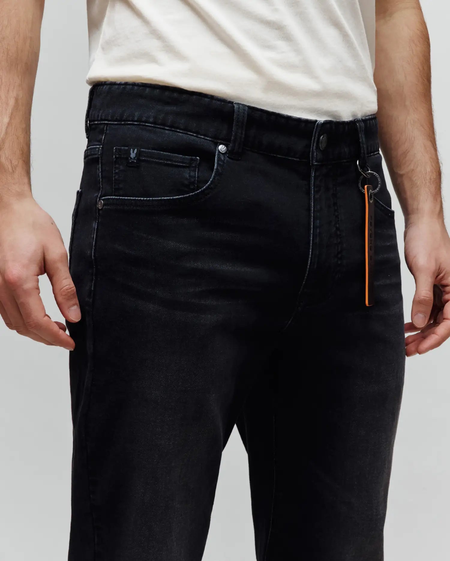 Mens Ace Knit Denim Pant in washed black, featuring a slim fit, small embroidered Psycho Bunny skull on the coin pocket, branded hardware, and an orange Psycho Bunny keychain.