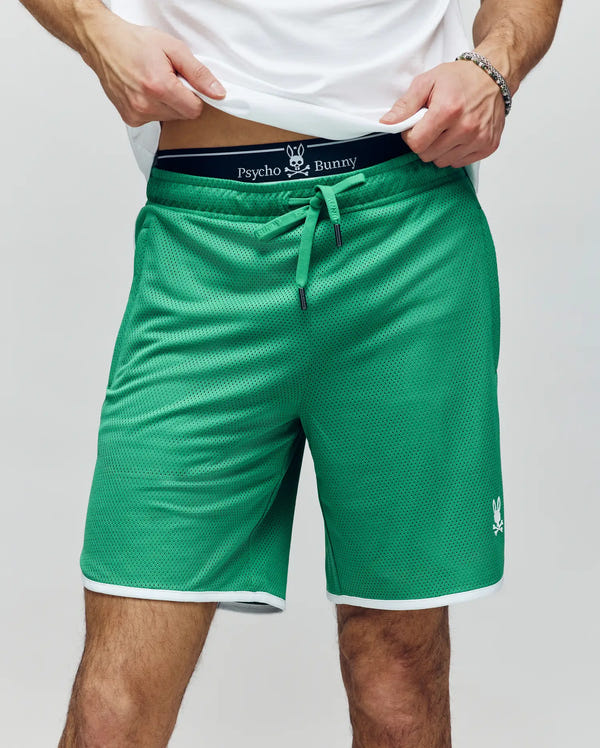 A person wears Psycho Bunny's MENS NICO MESH SHORT (MB0900004)—green with white trim and a bunny logo—styled with a visible Psycho Bunny underwear waistband and a white shirt. The breathable mesh fabric keeps them cool.