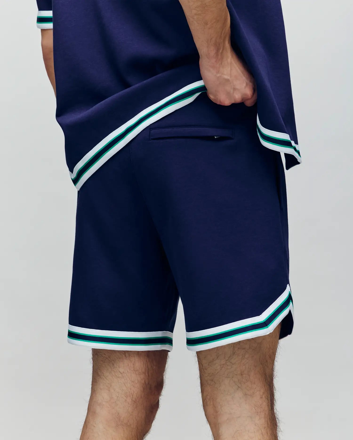 A person wearing Psycho Bunny’s MENS BASIL TAPED SHORT (MB0900005) with white and green striped trim stands confidently, hand on hip, highlighting the shorts’ back pocket.