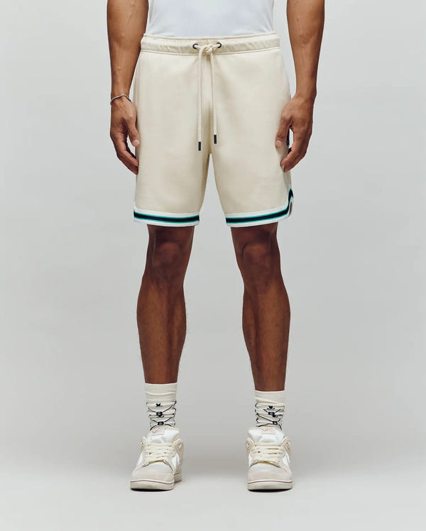 A person wears Psycho Bunny MENS BASIL TAPED SHORT - MB0900005, featuring a cotton-modal blend with teal and black trim, paired with white patterned socks and white sneakers, standing against a plain light background exuding classic confidence.