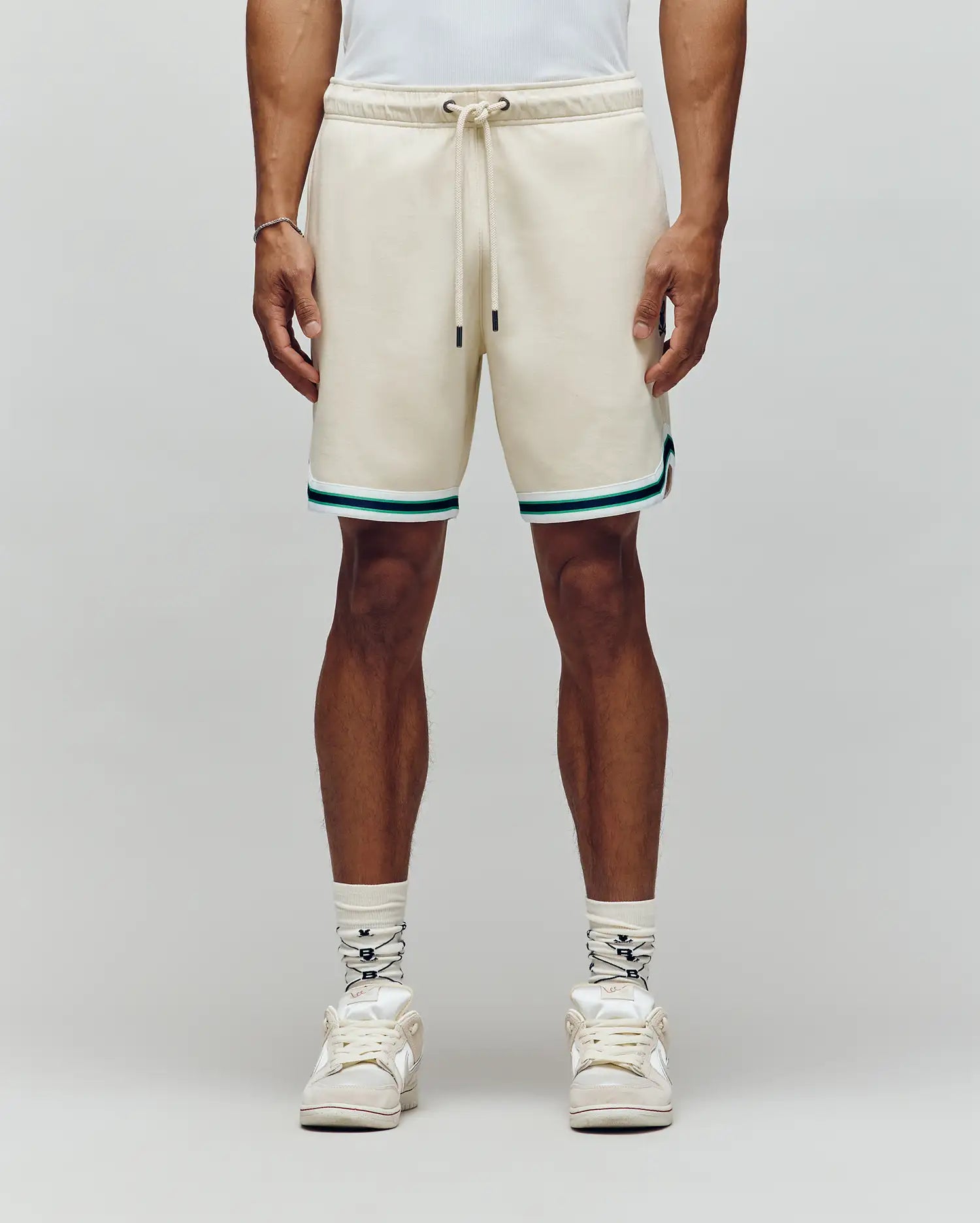 A person wears Psycho Bunny MENS BASIL TAPED SHORT - MB0900005, featuring a cotton-modal blend with teal and black trim, paired with white patterned socks and white sneakers, standing against a plain light background exuding classic confidence.