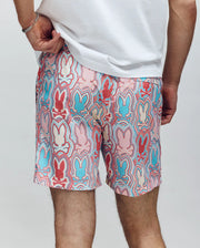 A person models Psycho Bunny’s MENS CHUCK ALL OVER PRINT LIGHTWEIGHT SWIM TRUNK (MB1000003), featuring recycled polyester and a vibrant red, blue, and pink bunny outline print, paired with a plain white tee.