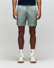 A person stands facing forward, showcasing only their lower half against a neutral background, wearing Psycho Bunny MENS ELIAS SWIM TRUNK - MB1000008 in a classic fit, styled with a black shirt, white crew socks, and white sneakers.