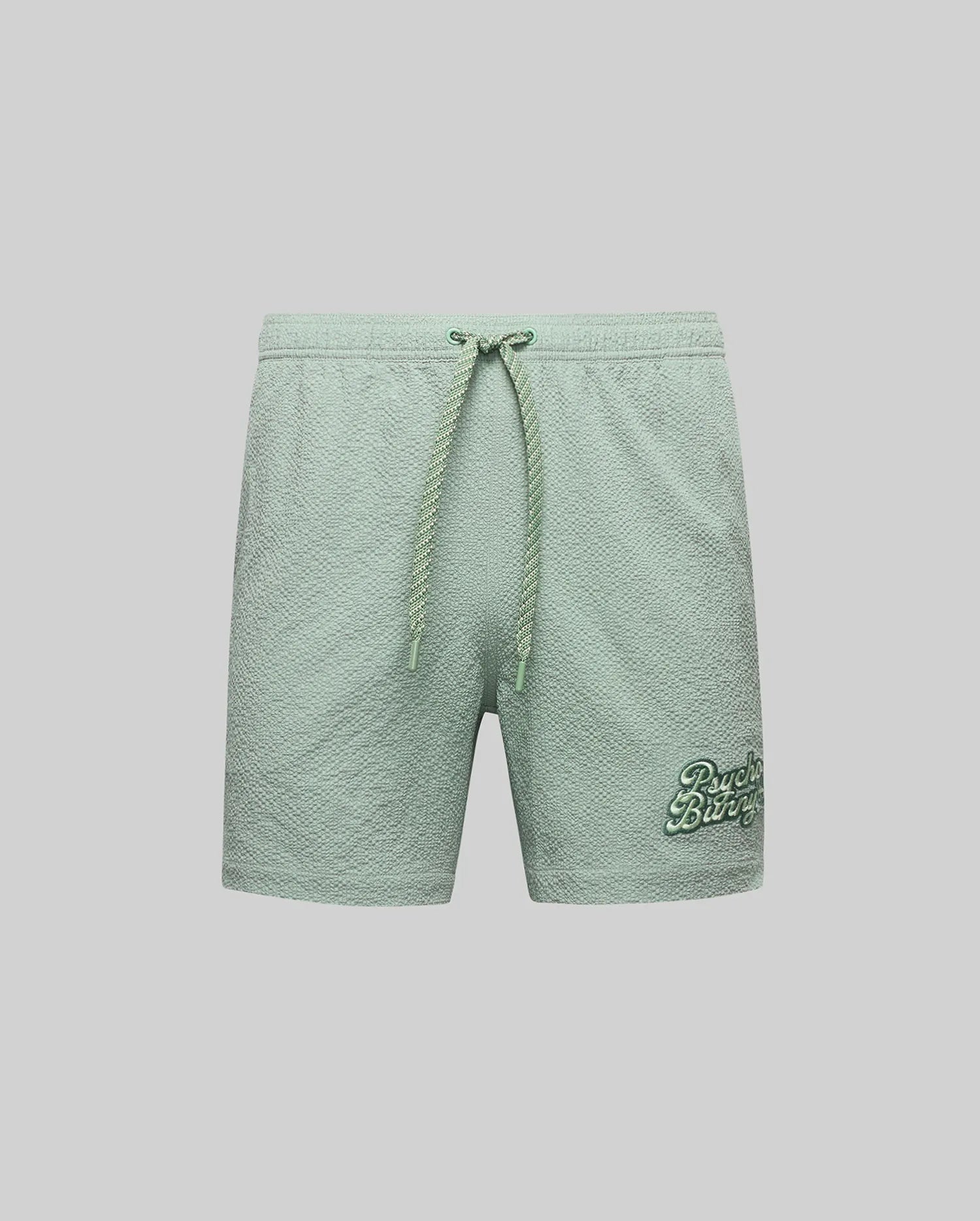 The Psycho Bunny MENS ELIAS SWIM TRUNK - MB1000008 features light green textured fabric, a classic fit, drawstring waistband, and darker green "Beach Bliss" embroidery on the lower left leg. Shown on a plain light gray background.