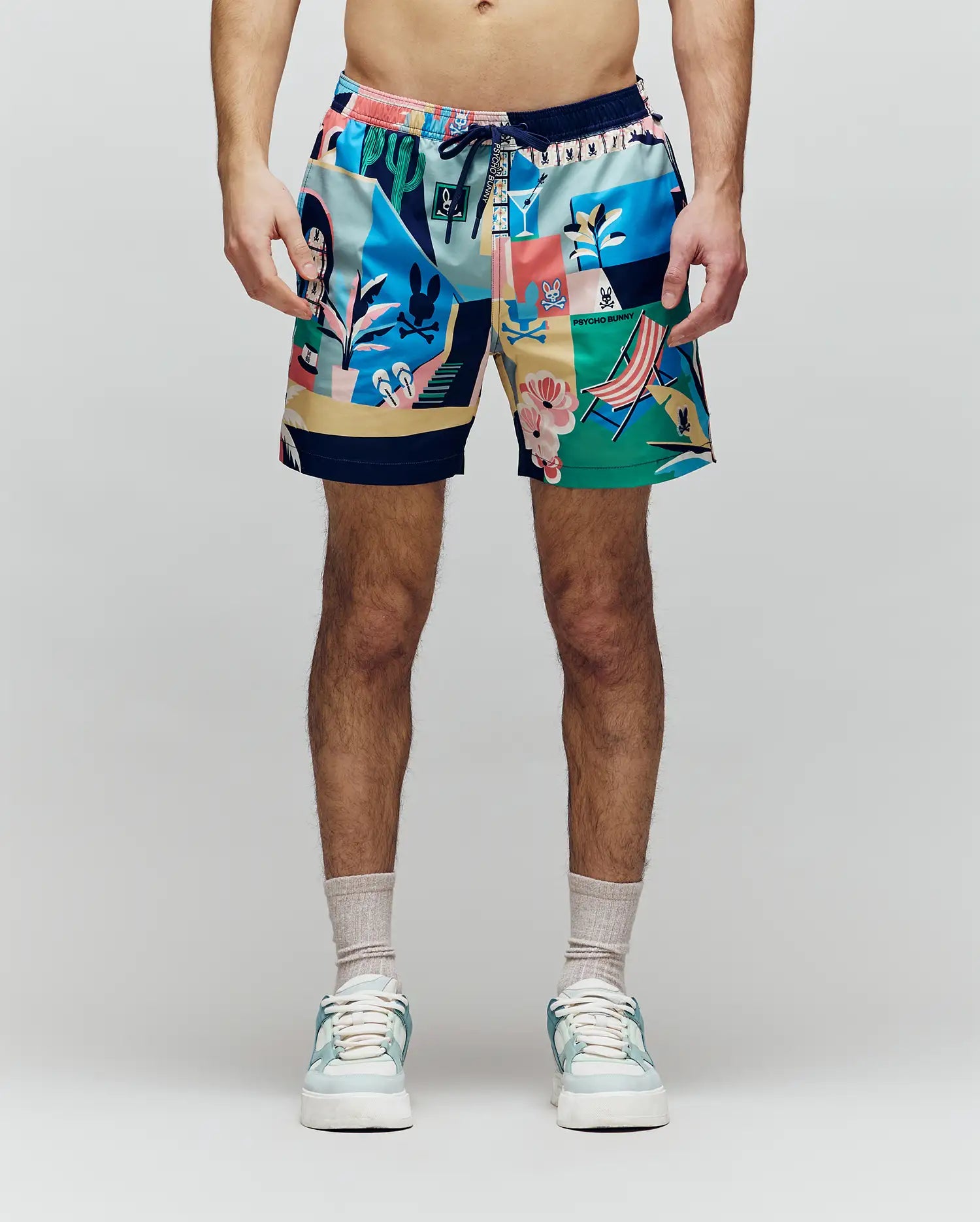 A person faces forward, shown from shoulders to feet against a light background, wearing Psycho Bunny MENS BLAISE SWIM TRUNK - MB1000028 with playful bunny logos, plus sandals and socks.