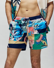 A person wears Psycho Bunny MENS BLAISE SWIM TRUNK - MB1000028, featuring a colorful tropical pattern with plants, beach chairs, cartoon rabbits, and bunny logos. Their hands are in their pockets beside a matching shirt.