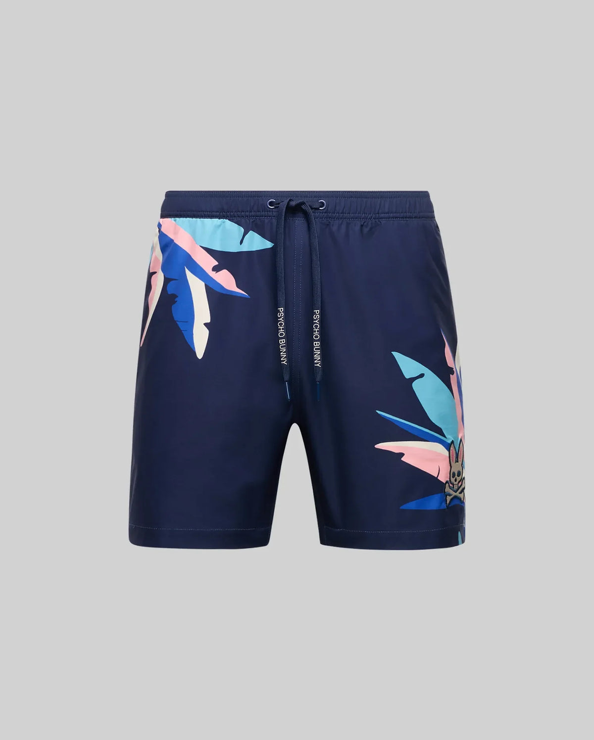 The Psycho Bunny MENS SHANE SWIM TRUNK - MB1000029 features a navy blue design with a drawstring waist and bold pink, blue, and white tropical leaf prints on the right leg and left hip, shown on a plain grey background.