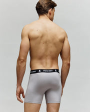 A man is seen from the back in Psycho Bunny's MENS 3 PACK BOXER BRIEF - MO1400006, light gray with a black waistband branded "PSYCHO BUNNY" and a white bunny logo. Made from a cotton-modal blend for comfort, set against a plain background.