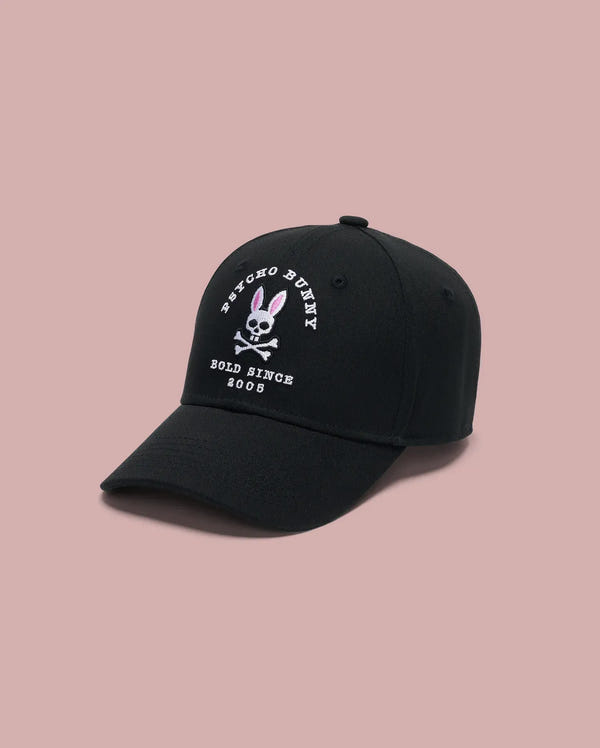 The Psycho Bunny MENS ARCHIVE BASEBALL CAP - MO1500002 is a black 100% cotton cap with the iconic embroidered bunny and crossbones logo plus "Bold Since 2005" on the front, shown on a light pink background.