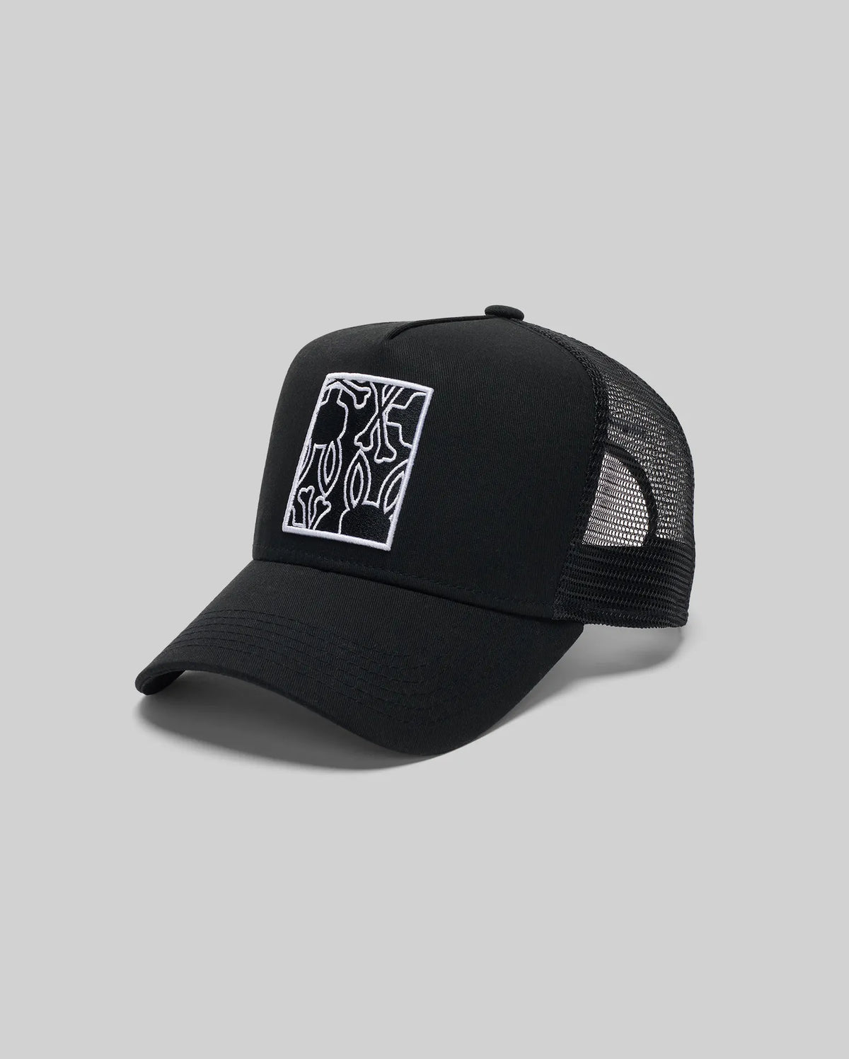 The Psycho Bunny MENS GLENN TRUCKER CAP (MO1500004) is a black trucker hat with mesh back, adjustable snapback, and a front square patch featuring a white-outlined abstract Bunny graphic, shown against a plain gray background.