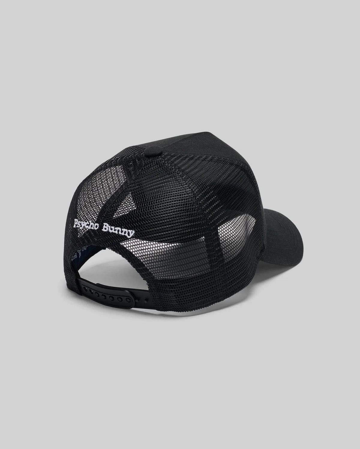 The Psycho Bunny MENS GLENN TRUCKER CAP (MO1500004) features black mesh, an adjustable snapback, and "Psycho Bunny" embroidered in white above the back opening. Shown against a plain gray background.