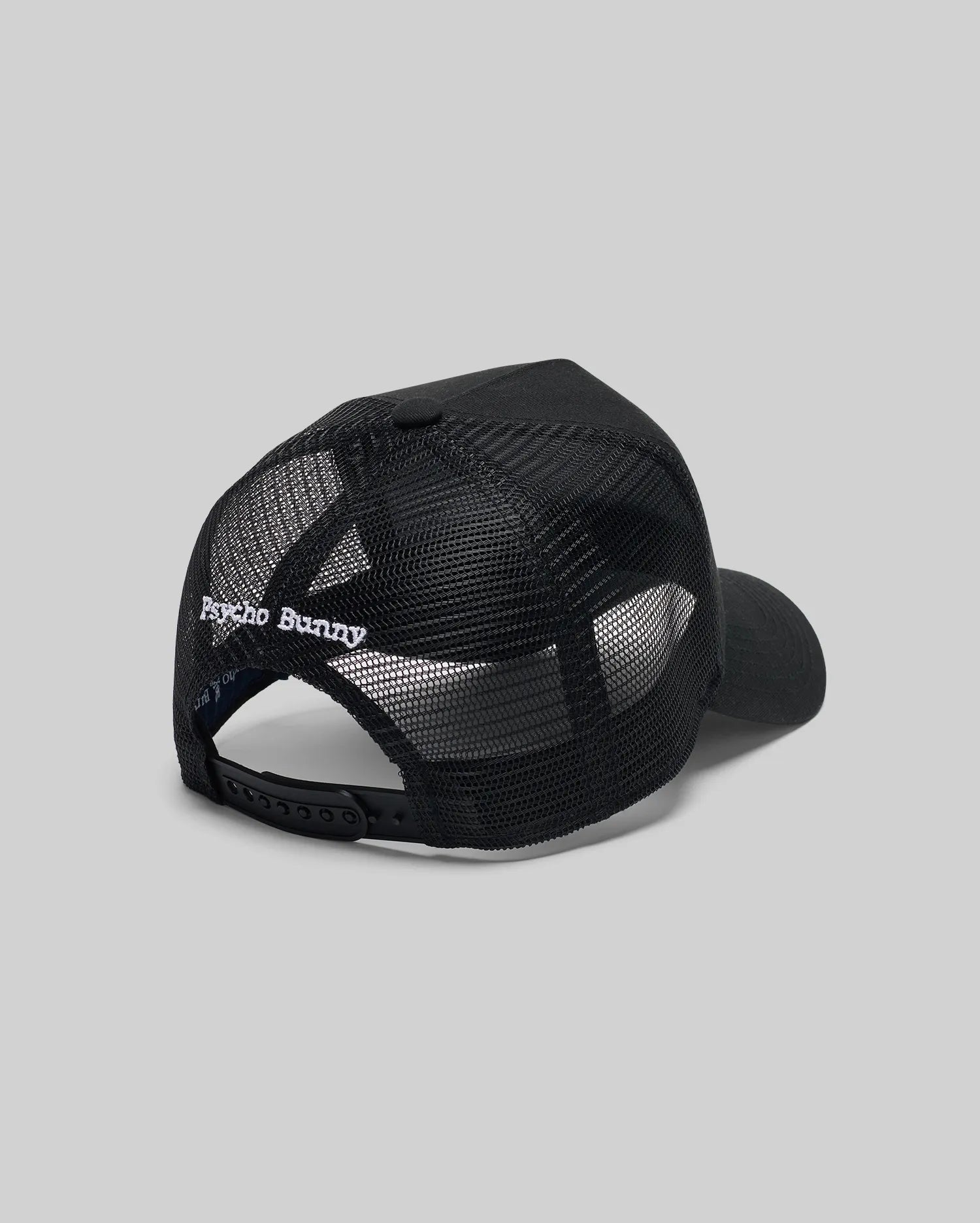 The Psycho Bunny MENS GLENN TRUCKER CAP (MO1500004) features black mesh, an adjustable snapback, and "Psycho Bunny" embroidered in white above the back opening. Shown against a plain gray background.