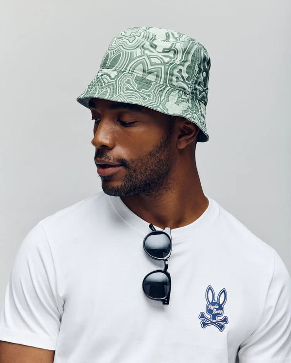 A man wears the Psycho Bunny MENS CHUCK REVERSIBLE BUCKET HAT (MO1500028) and sunglasses, flaunting the ideal summer accessory with SPF protection.