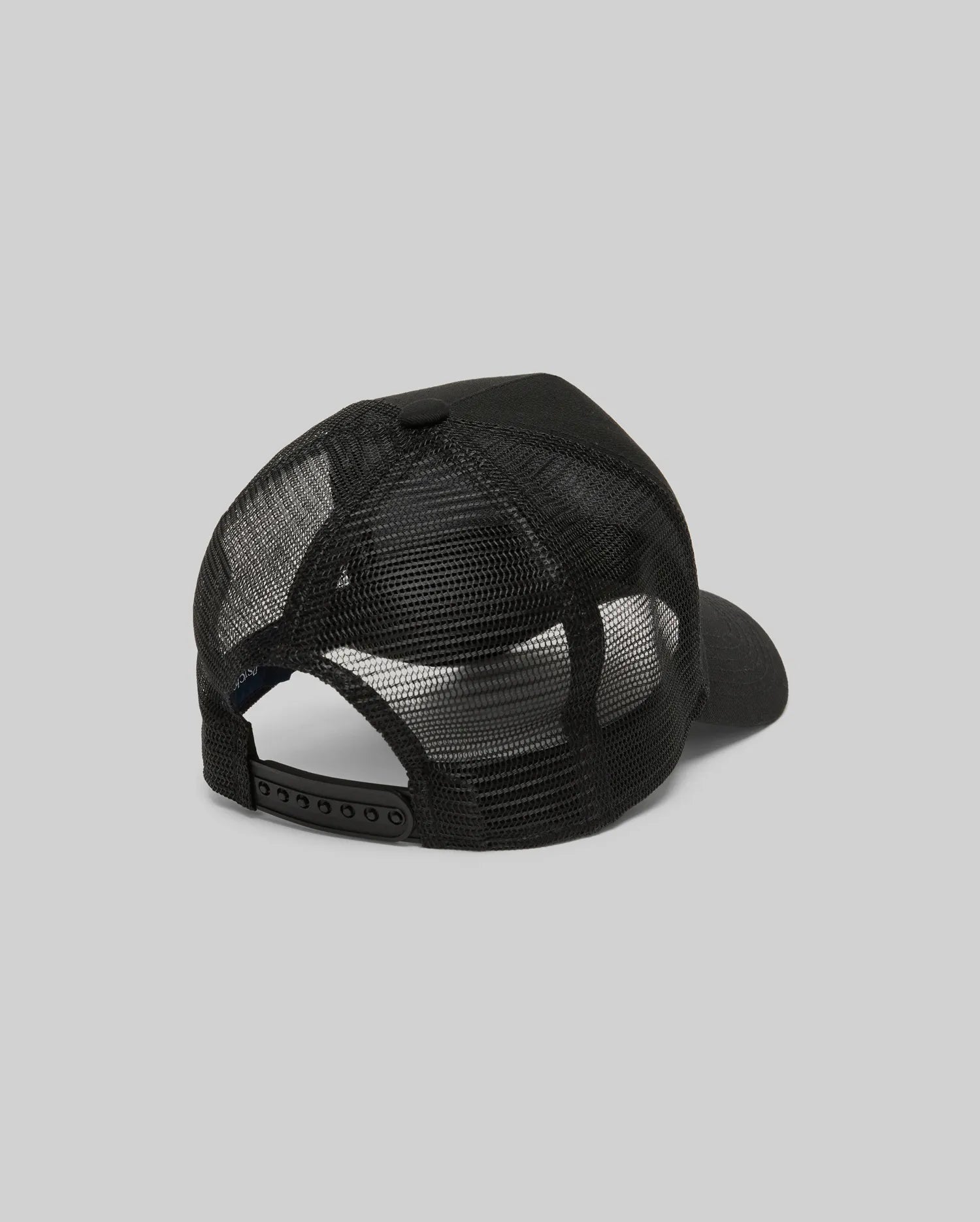 The Psycho Bunny MENS RYDER TRUCKER CAP (MO1500030) in black mesh and cotton twill is shown from the back, featuring an adjustable snapback closure and curved brim against a plain gray background.