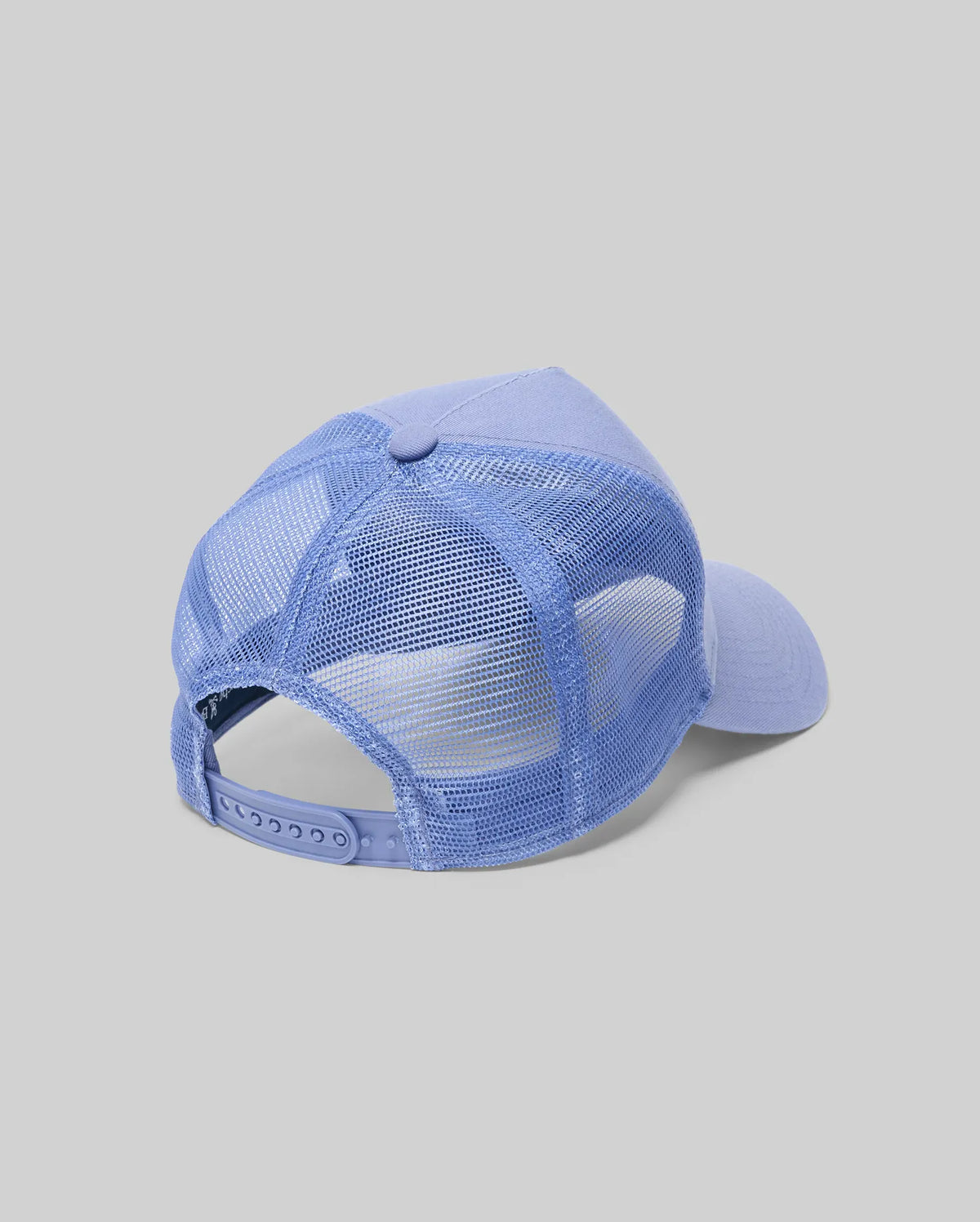 The Psycho Bunny MENS RYDER TRUCKER CAP (MO1500030), in light blue cotton twill with a mesh back and adjustable snapback, is shown angled to display its back and side against a plain gray background.