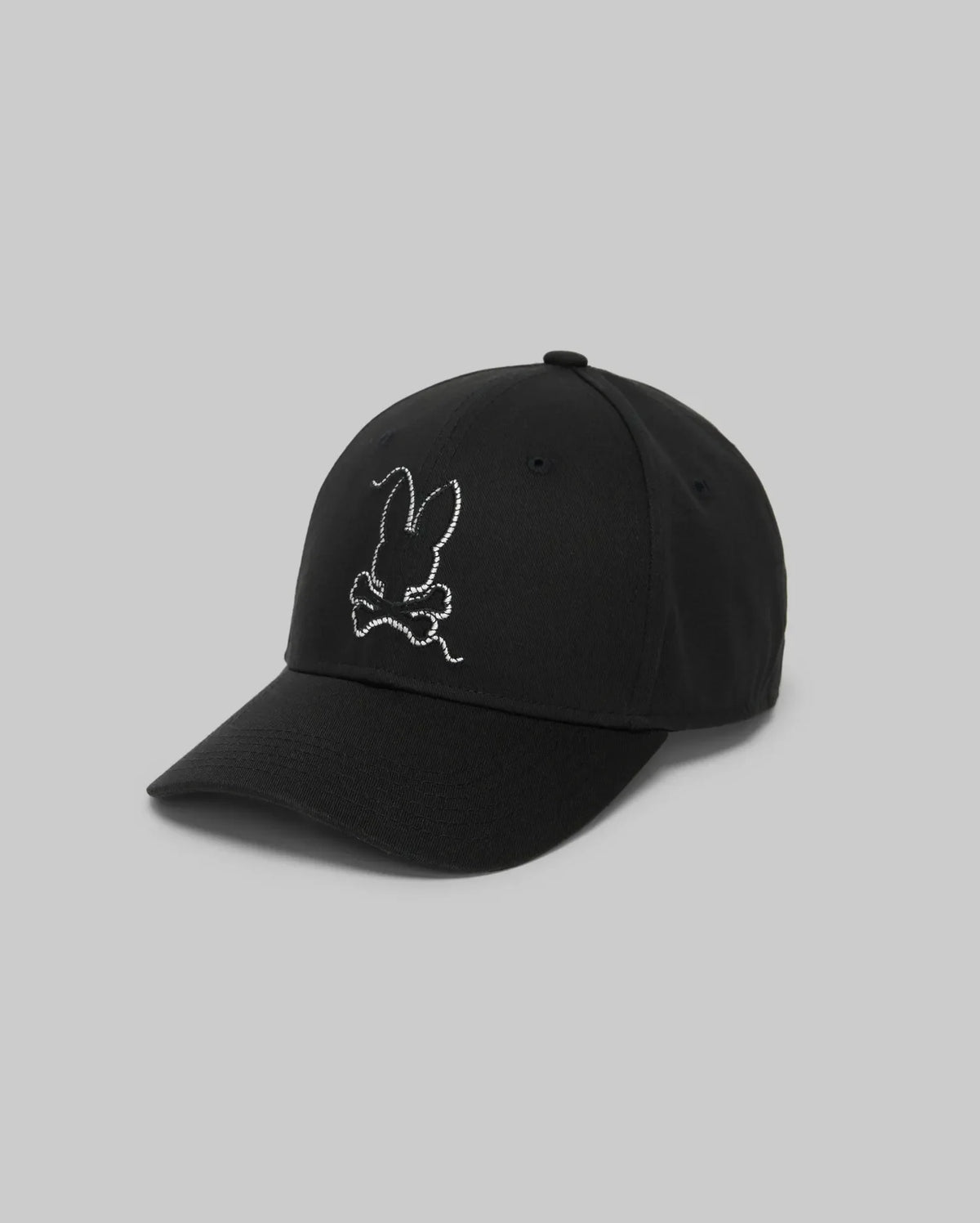 The Psycho Bunny MENS CYRUS BASEBALL CAP - MO1500045 is a black cap with an embroidered white bunny head above crossed bones on the front, styled for subtle coastal charm against a plain light gray background.